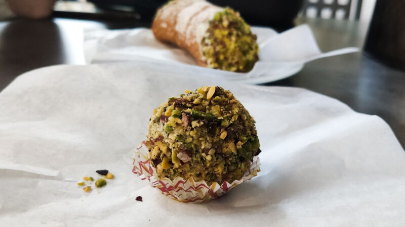 Pistacchio ball on a plate, in the background a cannolo